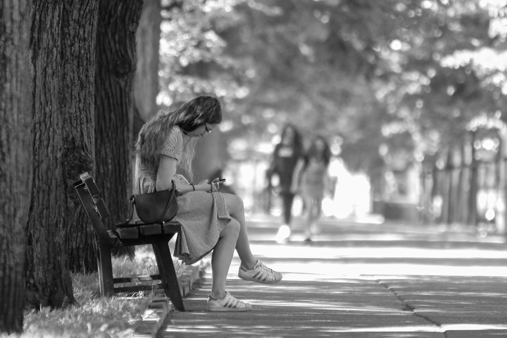 A woman sitting on a park bench with her phone